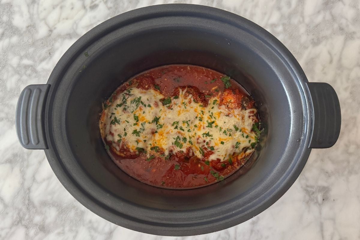 Chicken parmesan in the slow cooker topped with cheese and parsley.