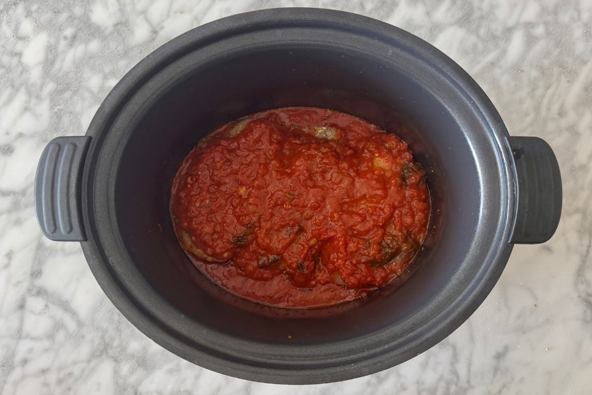 Marinara sauce covering chicken in a slow cooker.