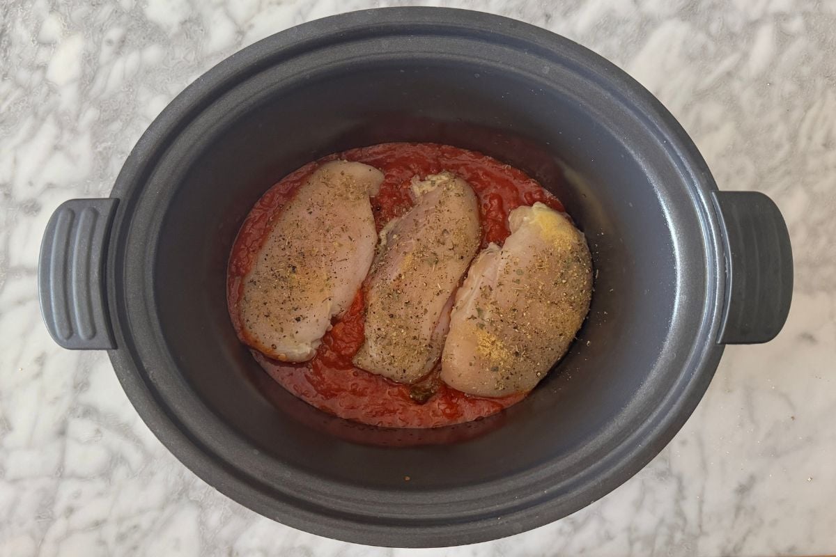 Seasoned chicken and marinara sauce in a slow cooker.