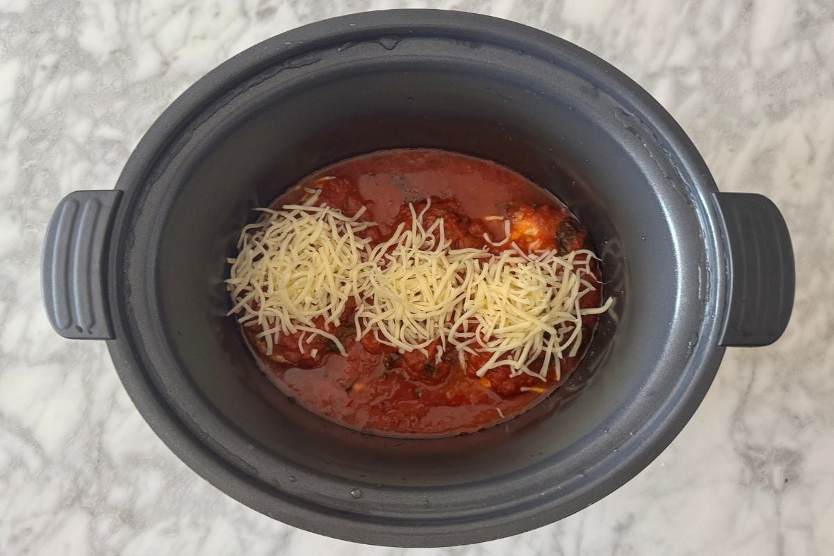 Shredded cheese over chicken parmesan in slow cooker.