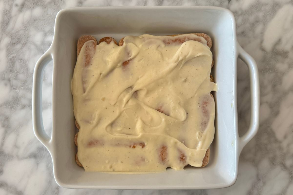 Eggnog filling spread on ladyfingers in dish