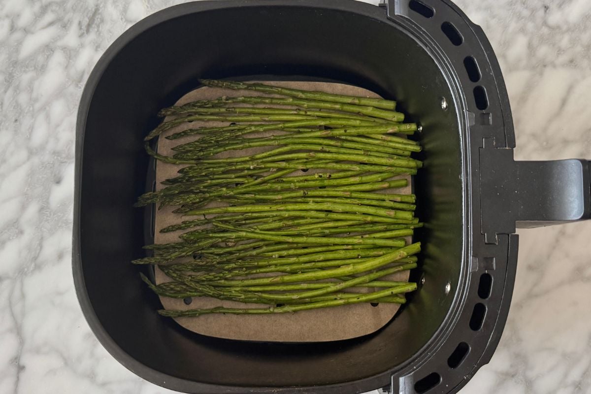 Seasoned asparagus in the air fryer basket.
