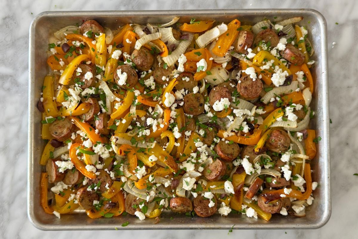 Baked sausage and peppers on a sheet pan topped with feta cheese.