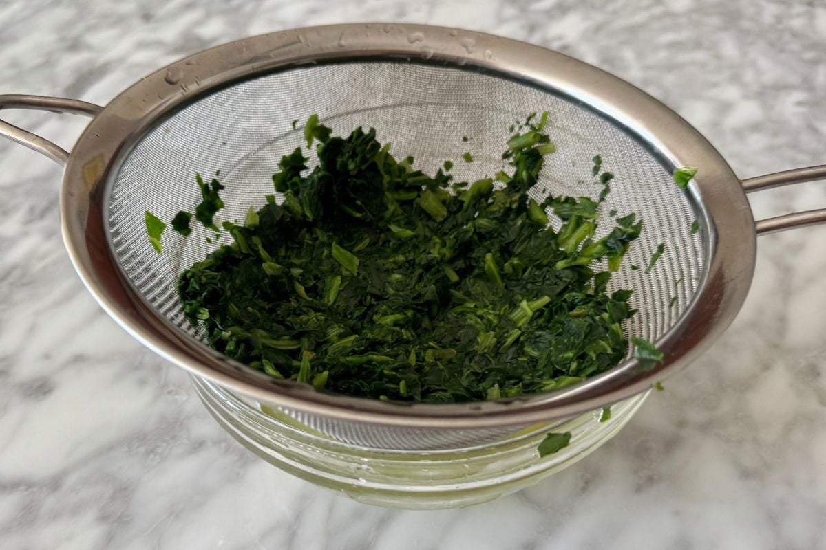 Drained frozen spinach in a strainer over a bowl.