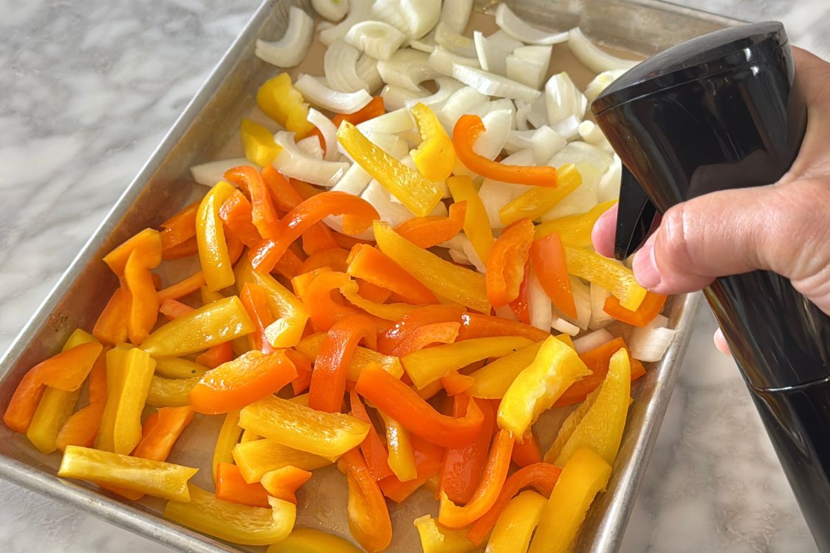 Sliced bell peppers and onions on a sheet pan.