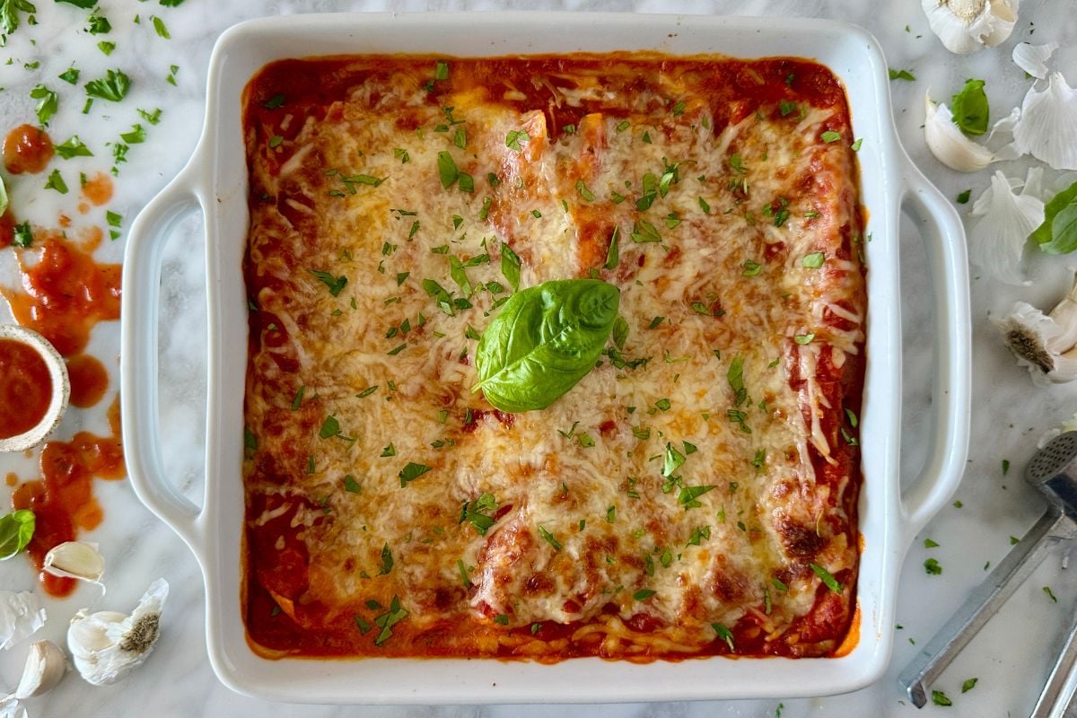 Spinach lasagna topped with fresh basil in baking dish.
