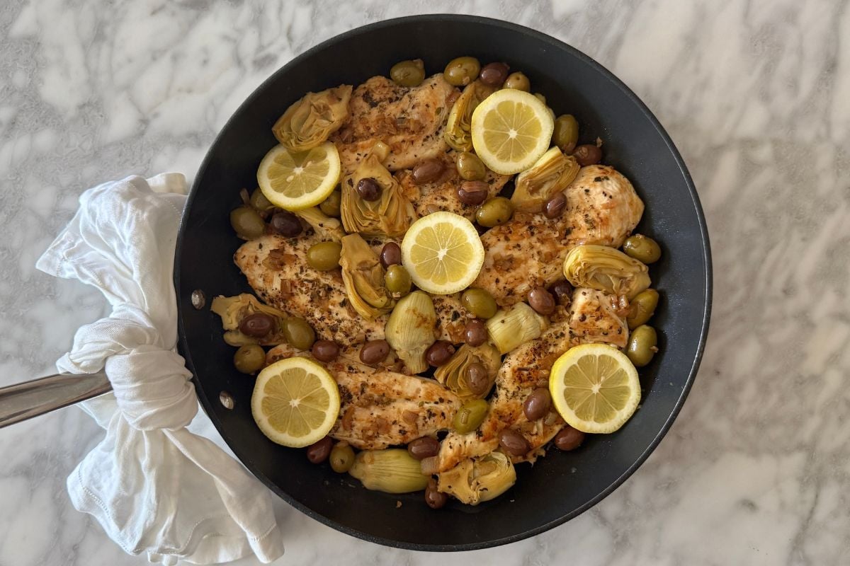 Cooked chicken with artichokes and olives served in a pan.