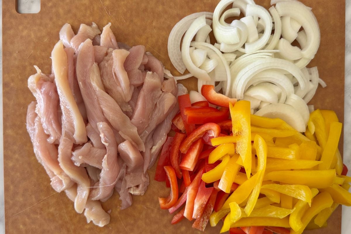 Sliced chicken bell peppers and onions on cutting board.