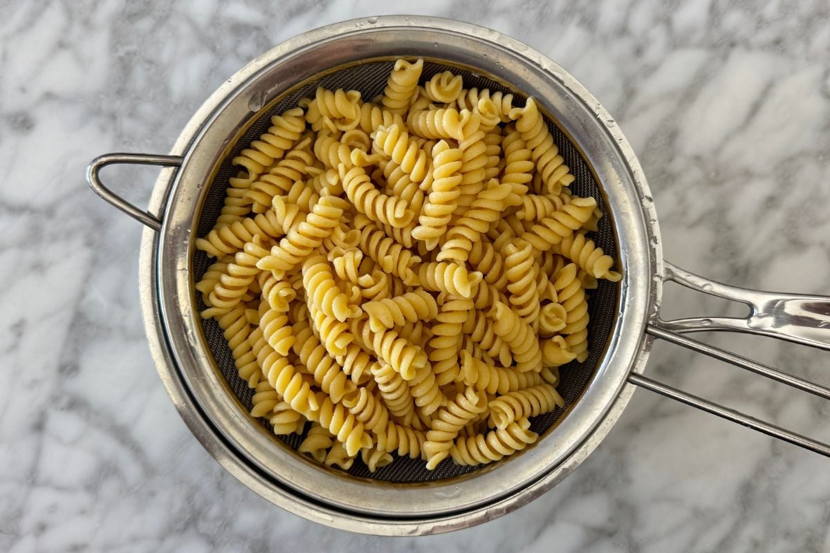 A metal colander filled with cooked fusilli pasta on a marble countertop