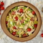 Bowl of chicken pasta salad with fusilli, lettuce, cherry tomatoes and shredded cheese, garnished on a marble surface.