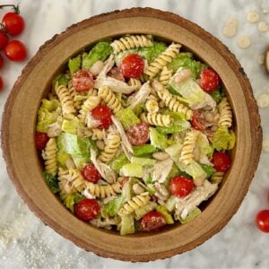 Bowl of chicken pasta salad with fusilli, lettuce, cherry tomatoes and shredded cheese, garnished on a marble surface.