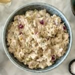 Bowl of creamy chicken salad with diced red onions and pickles, surrounded by prep bowls of onions and spices on a light countertop