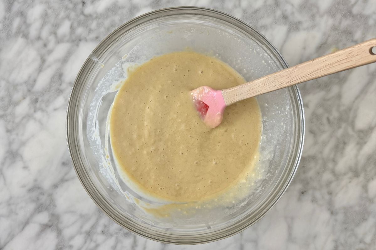Muffin batter in a bowl | Healthy Foodie Girl Top-down view of a glass mixing bowl with light brown batter and a pink silicone spatula resting inside.