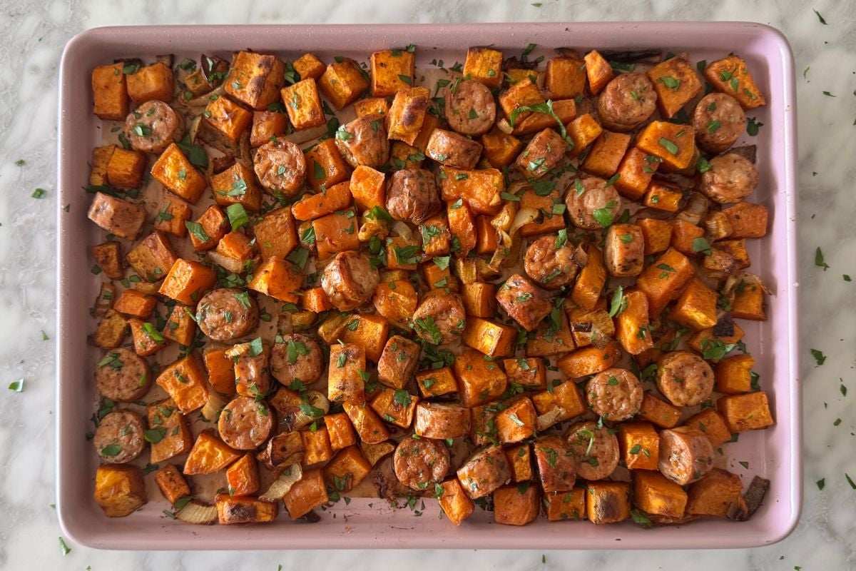 Sausage and sweet potatoes on a sheet pan topped with parsley.