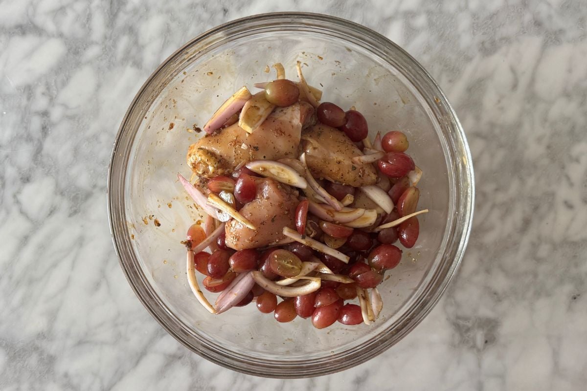 Coated chicken thighs shallots and grapes in bowl.