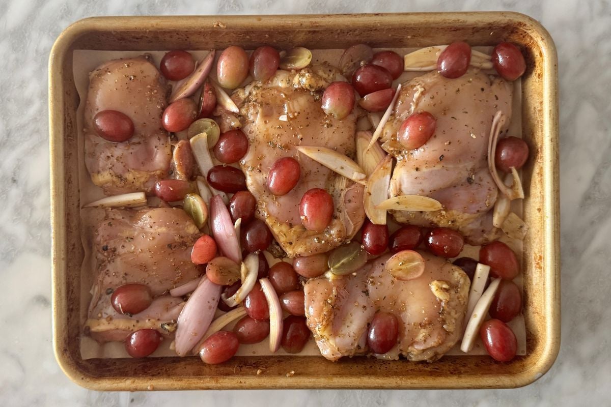 Coated chicken with grapes and shallots on sheet pan.