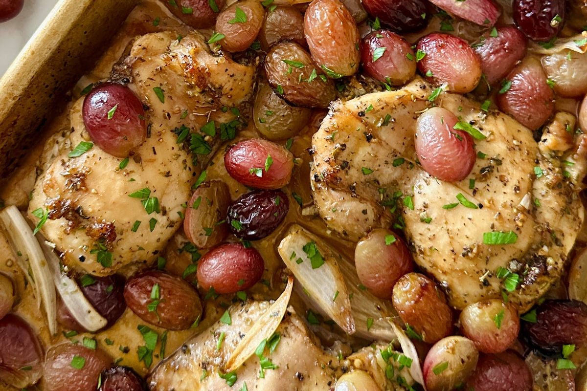 Roasted chicken thighs with grapes and shallots on a sheet pan.