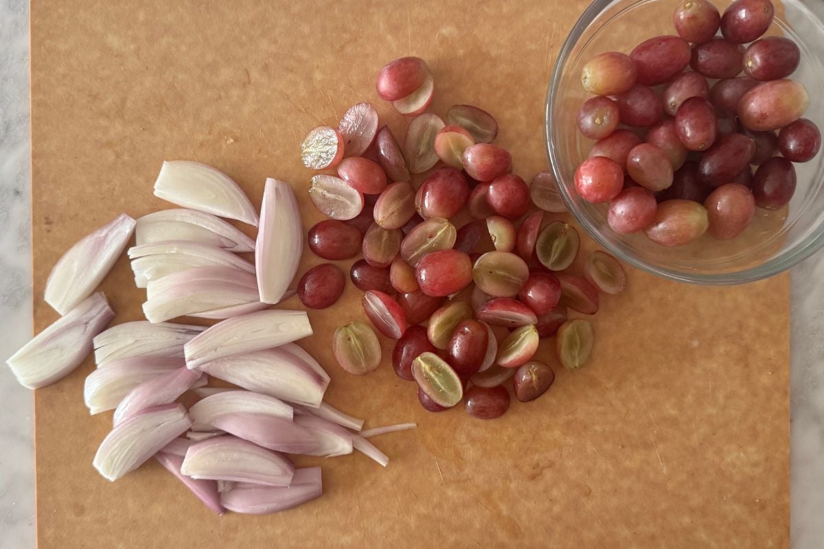 Sliced shallots and grapes on cutting board.