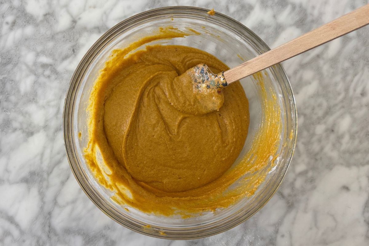 Golden turmeric paste in a glass bowl with a wooden spoon resting on a marble countertop.